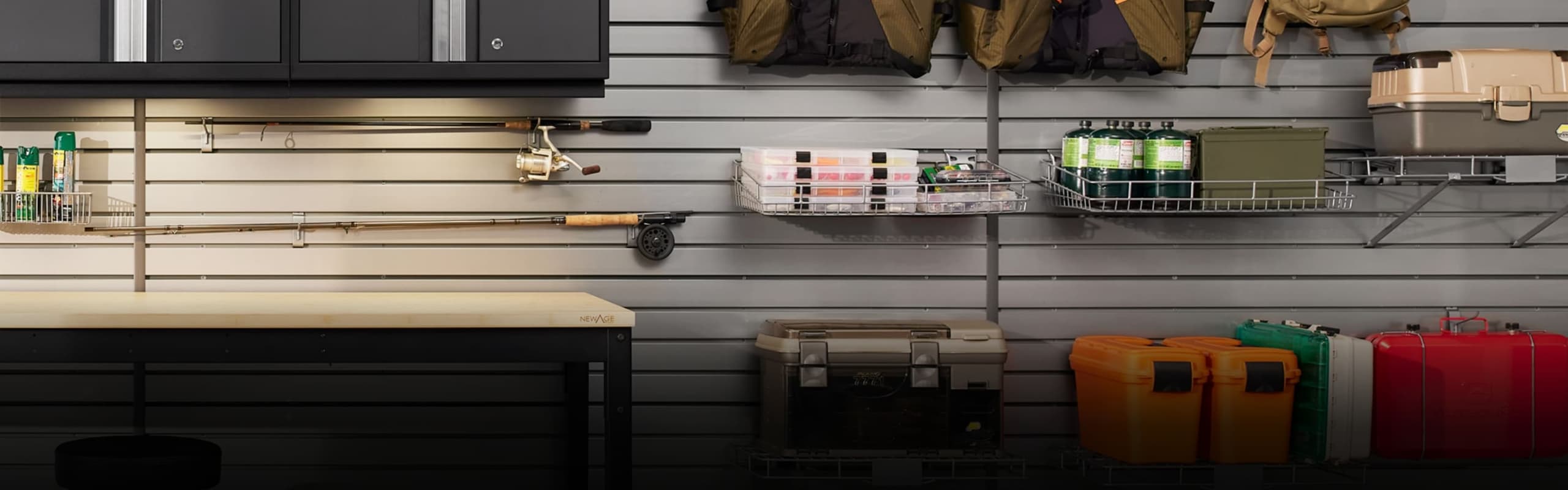 Grey slatwall holding fishing rods, life jackets, tackle boxes and baskets above a workbench