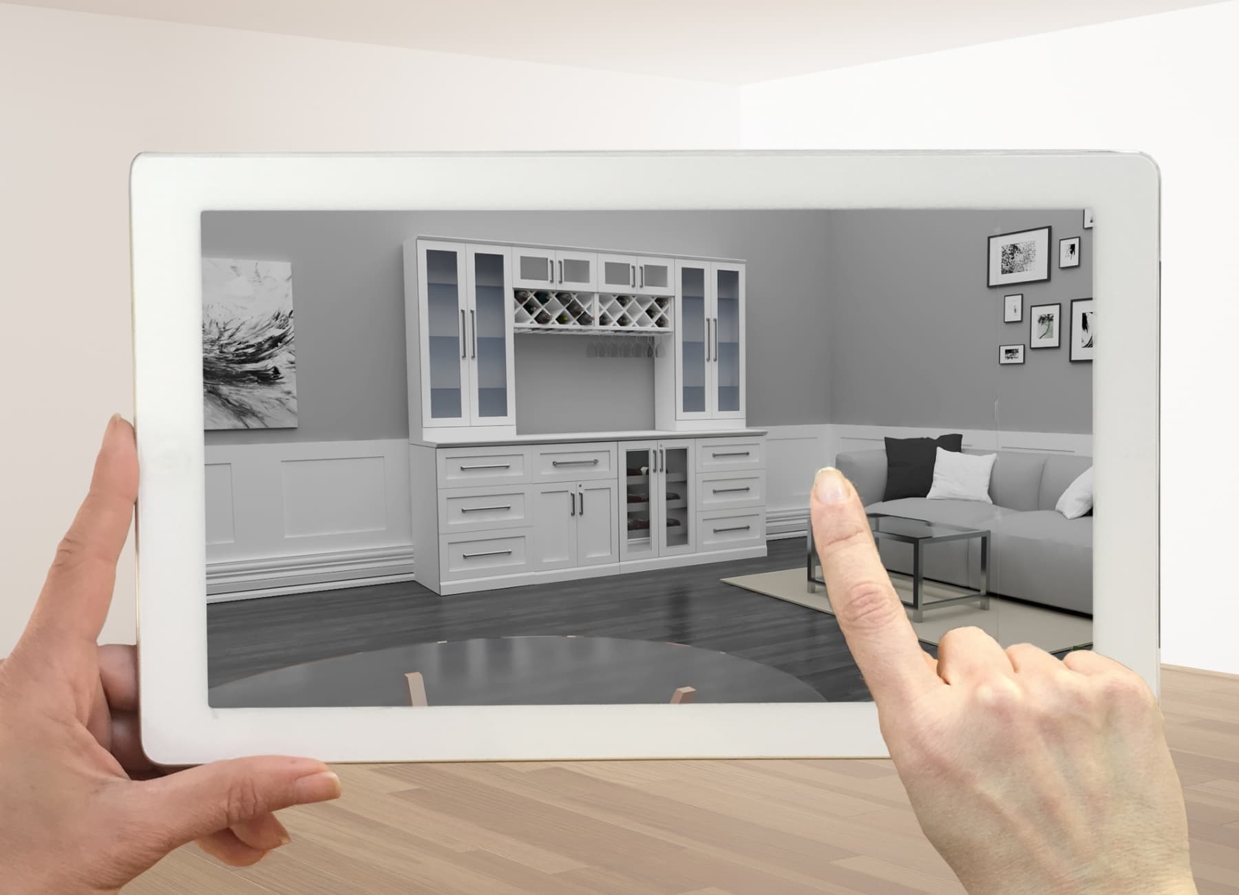 A hand holding a tablet displaying a 3D rendering of a white home bar cabinet in a living room, illustrating the virtual design planning process.