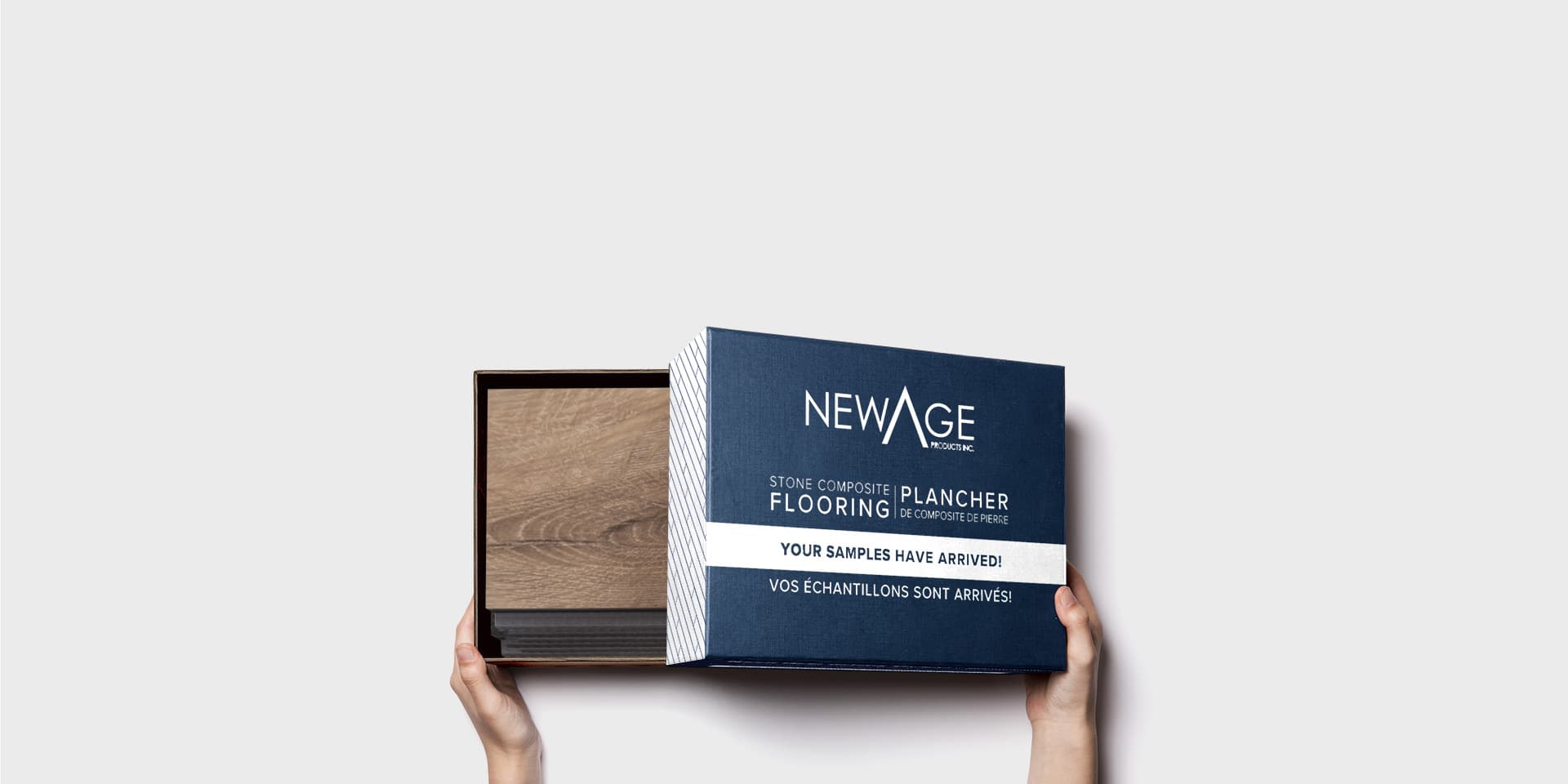 Hands holding an open NewAge stone composite flooring sample box with a wood-look swatch inside