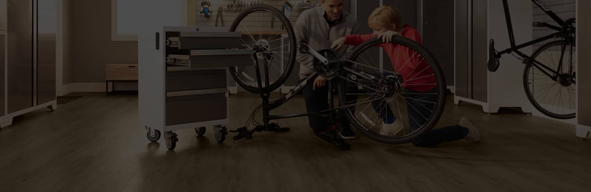 A father and son repairing a bicycle in a garage with dark wood-look luxury vinyl plank flooring.