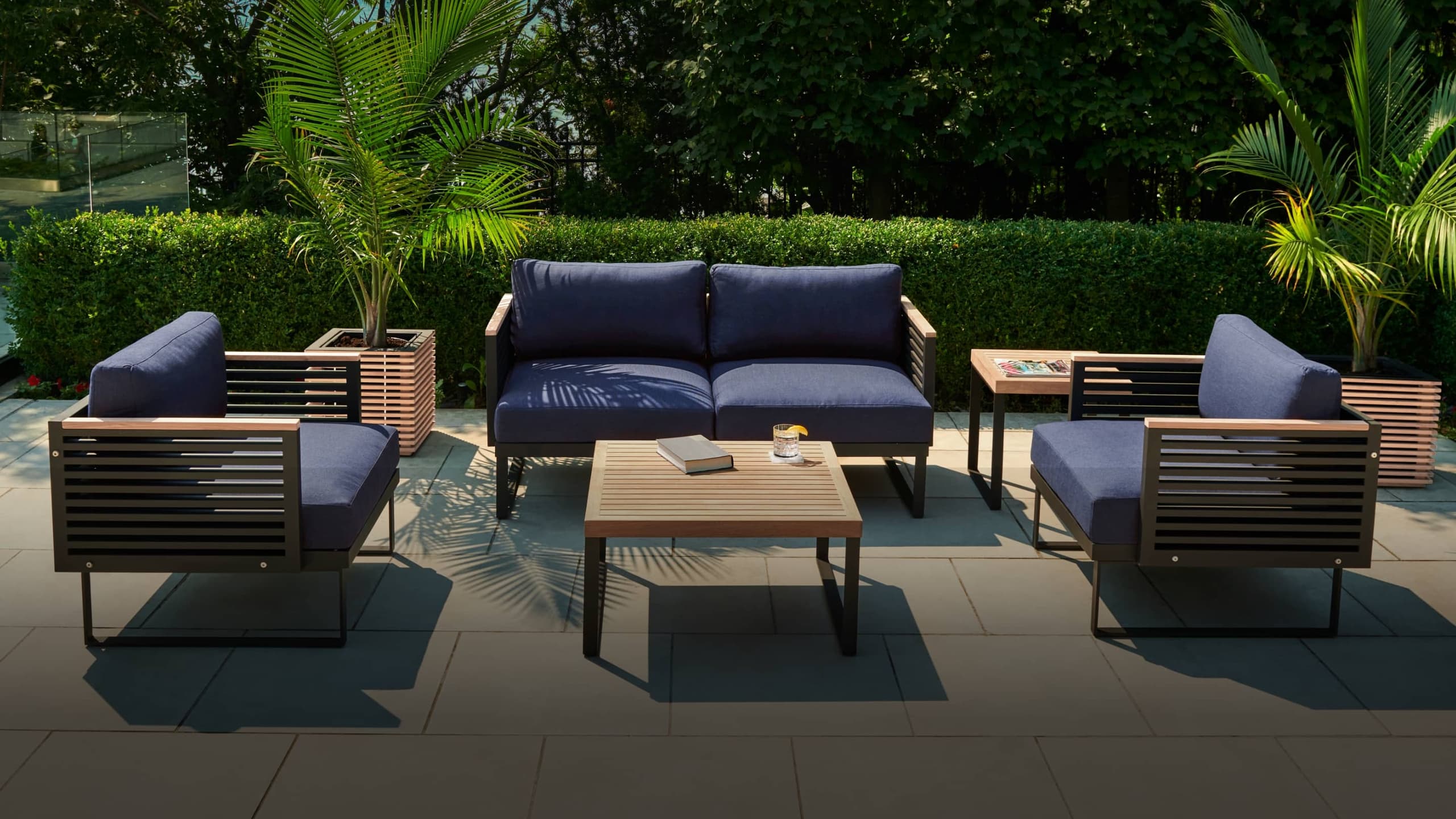 NewAge teak outdoor sectional, ottoman and coffee tables on a poolside patio