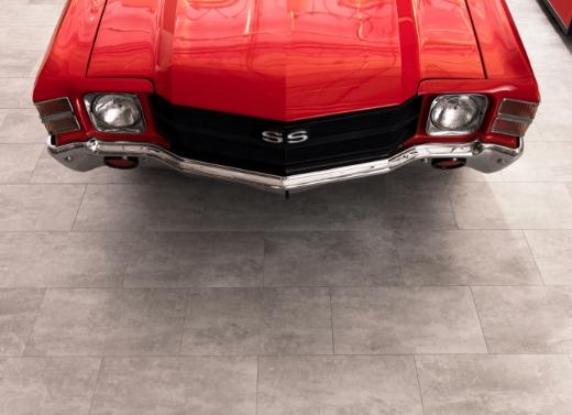 A luxurious garage showcases a parked red muscle car. The image highlights Stone Composite Luxury Vinyl Tiles and Planks.