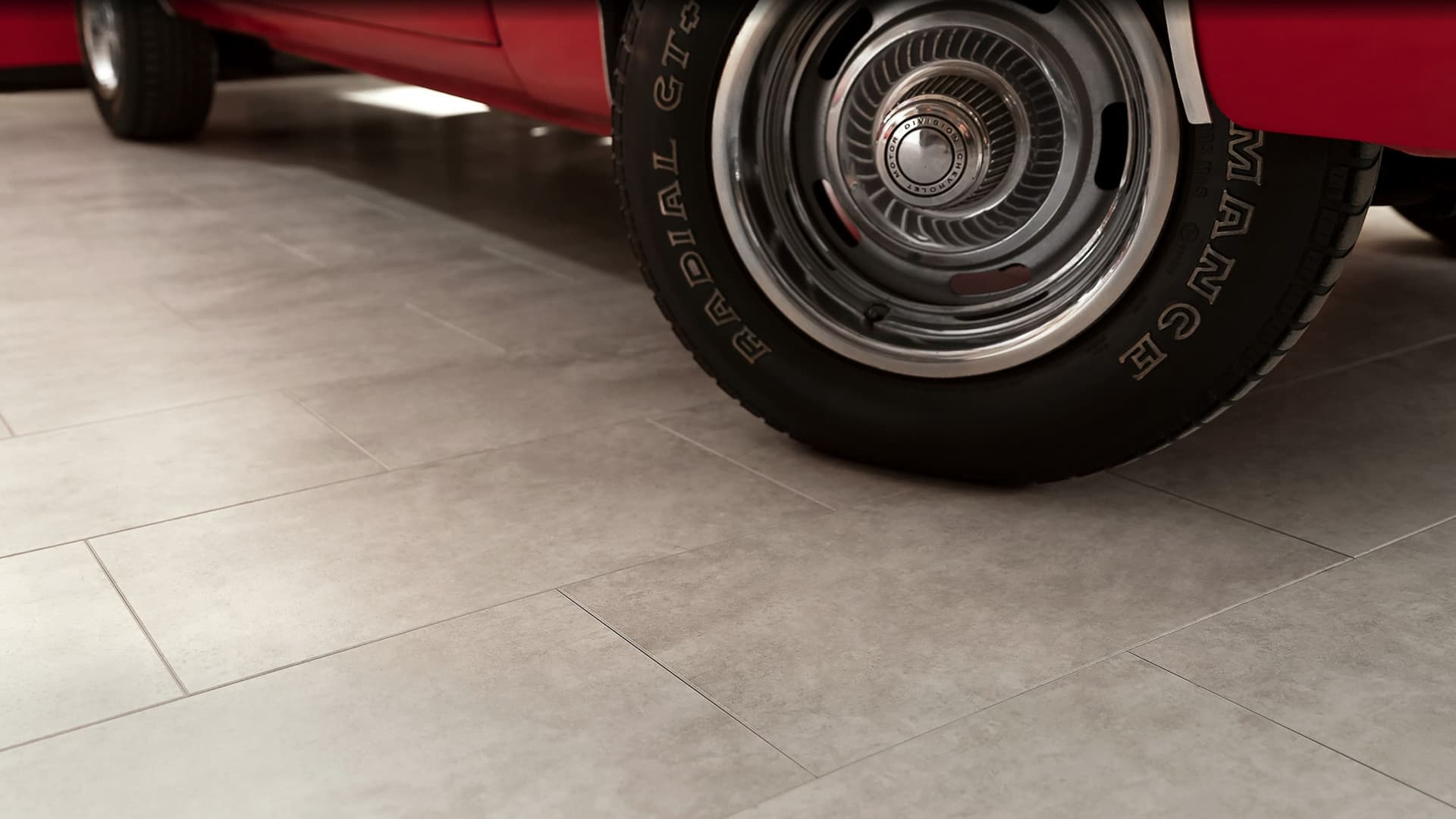 Close-up of grey NewAge garage floor tiles beneath the wheel of a red classic car