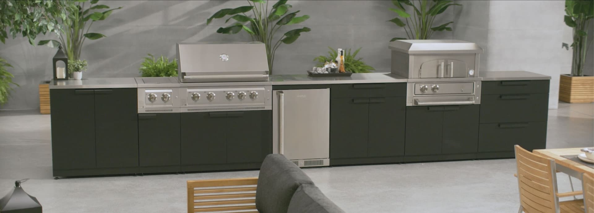 A long NewAge outdoor kitchen run in matte black with a stainless built-in gas grill, side burner, outdoor fridge and countertop pizza oven