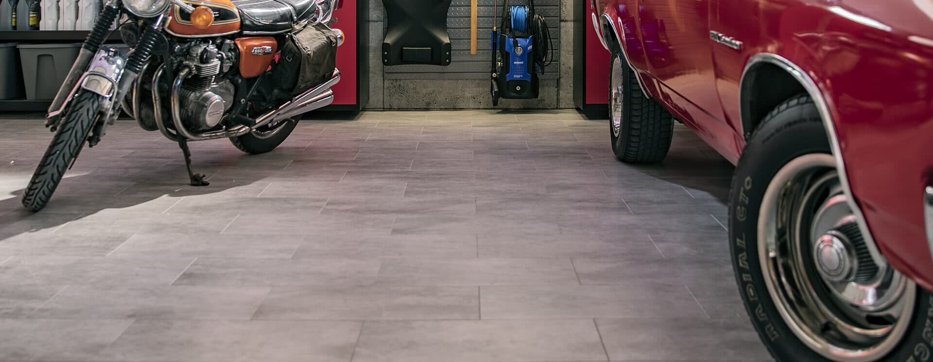 A vintage motorcycle and red classic car on gray vinyl tile flooring, red cabinetry