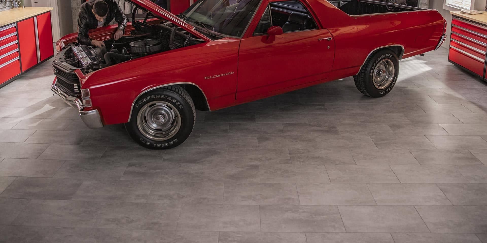A red classic El Camino, hood open, on gray vinyl tile flooring in a red-cabinet garage