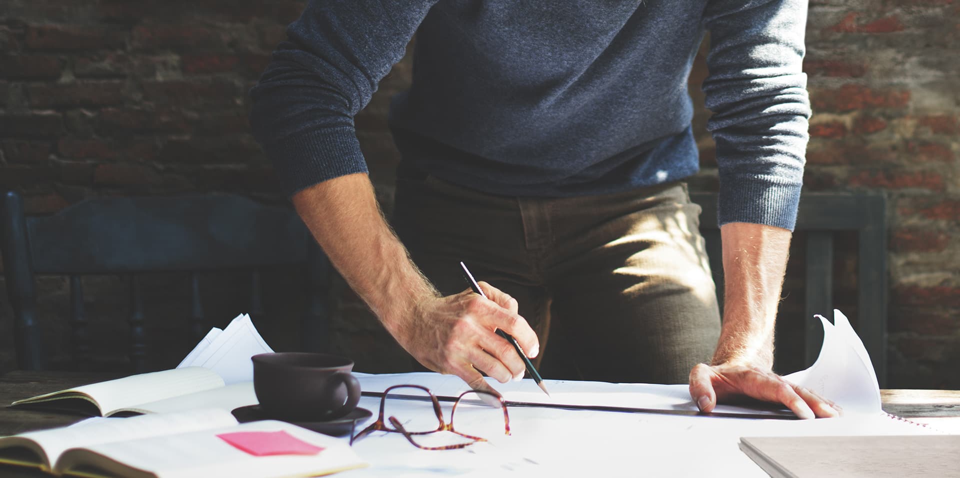 Man's hands sketching blueprint plans at a desk with a notebook and coffee