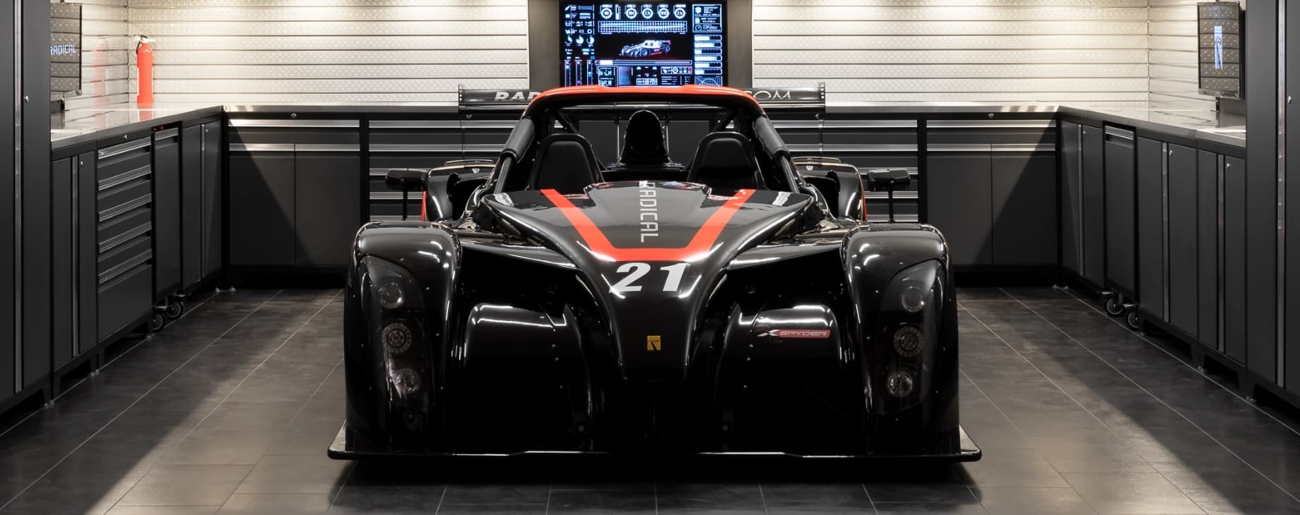 A black and red racing car in a showroom-style garage with dark tiles and cabinets