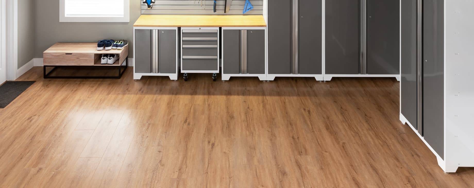 Wood-look vinyl plank flooring in an entryway with gray cabinets and a shoe bench