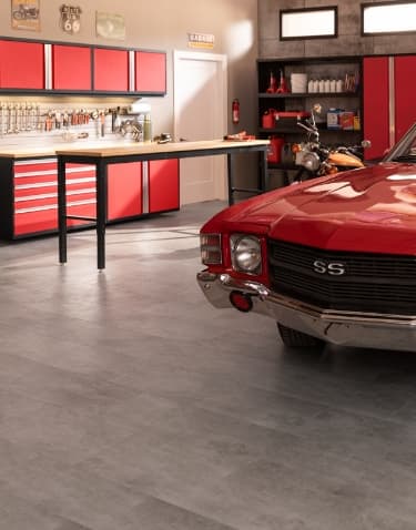 A red vintage muscle car on gray tile flooring, with red cabinets, workbench and motorcycle
