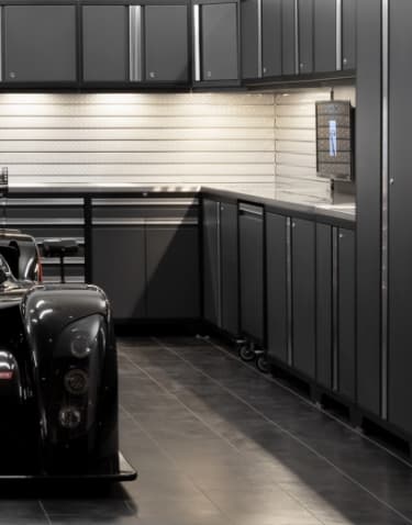 A black and red racing car in a showroom-style garage with dark tiles and cabinets