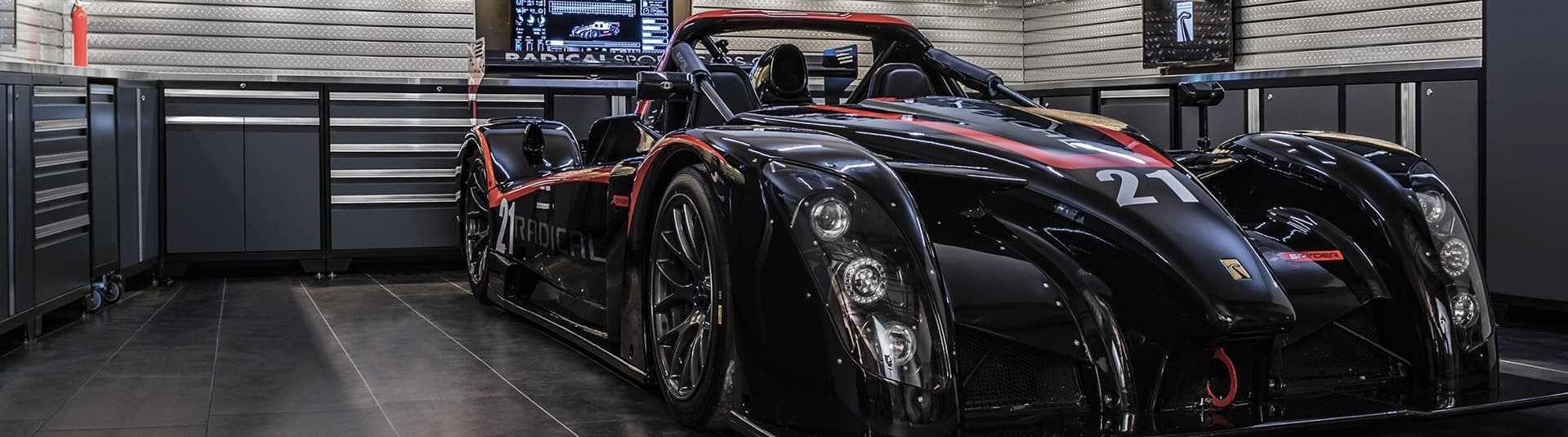 Black and red sports car parked in a garage with dark gray NewAge cabinets