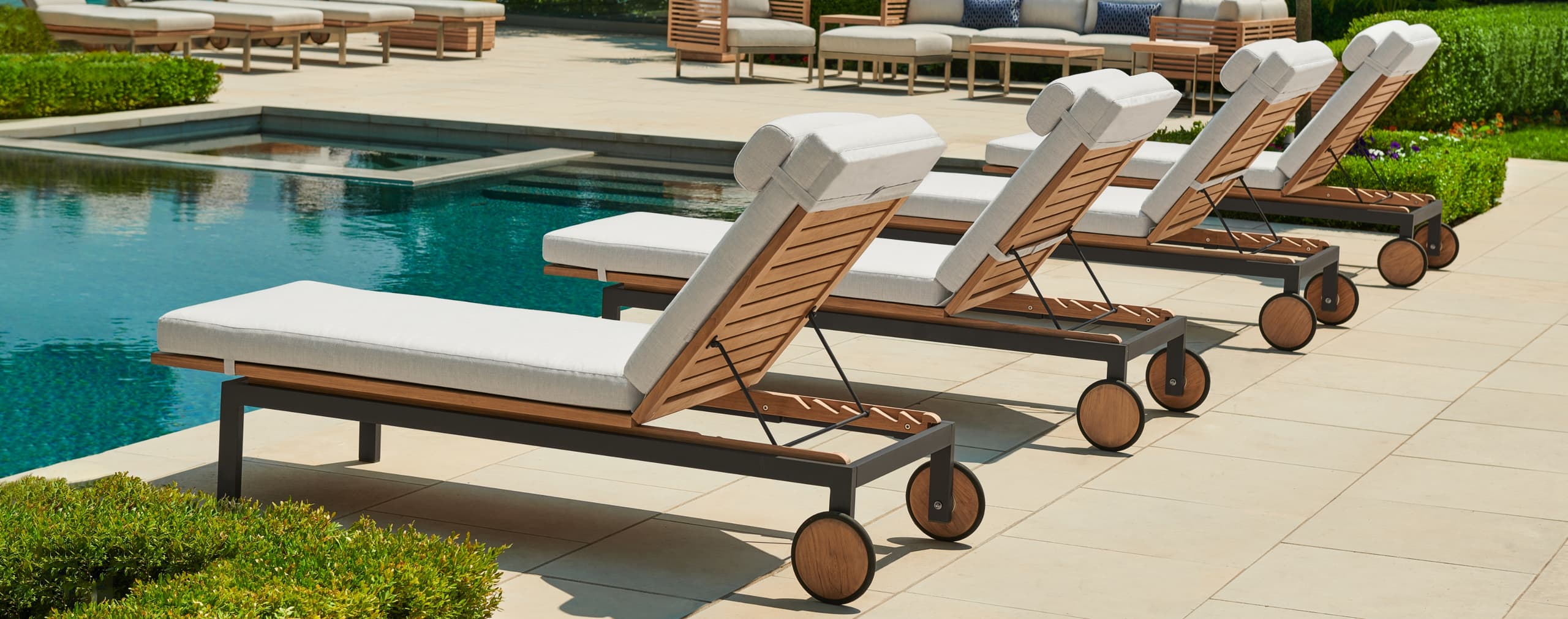 Row of teak chaise lounges with white cushions beside a pool