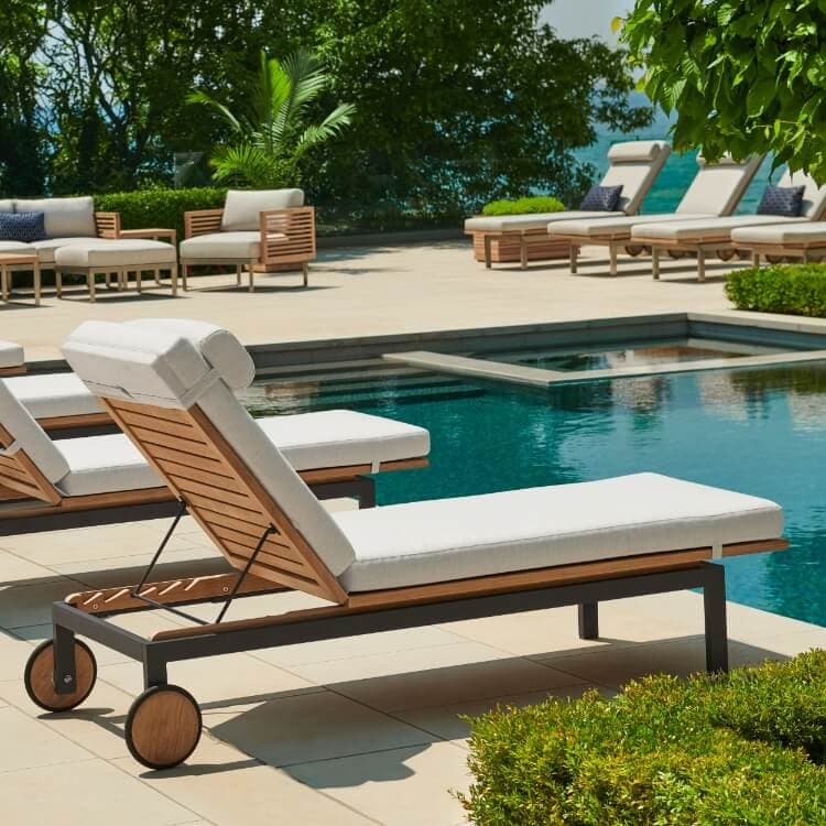 Row of teak chaise lounges with white cushions beside a pool